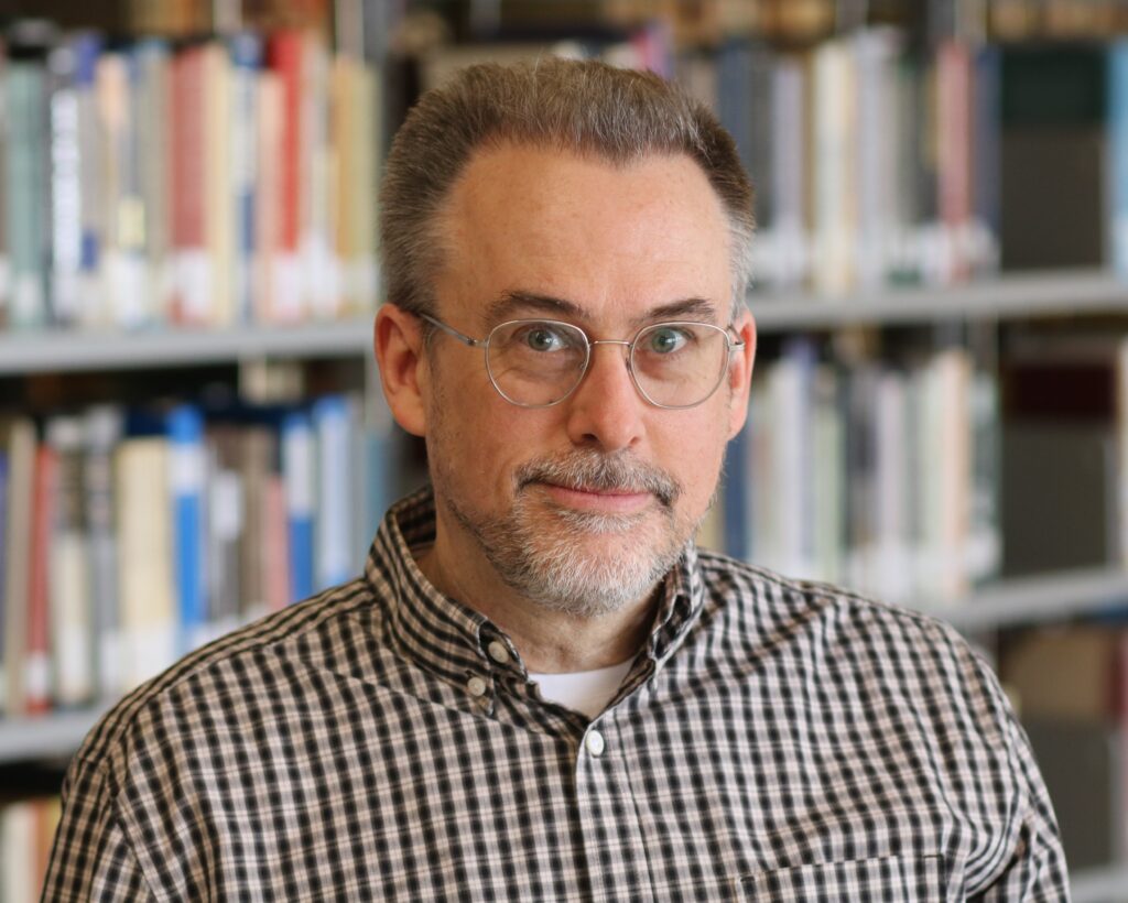 Photo of author Michael Dudley standing before a shelf of books.